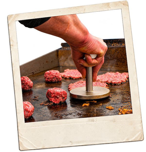 A hand pressing a round metal smasher down onto fresh patties on the Crack Burger flat-top griddle, printed as a retro polaroid